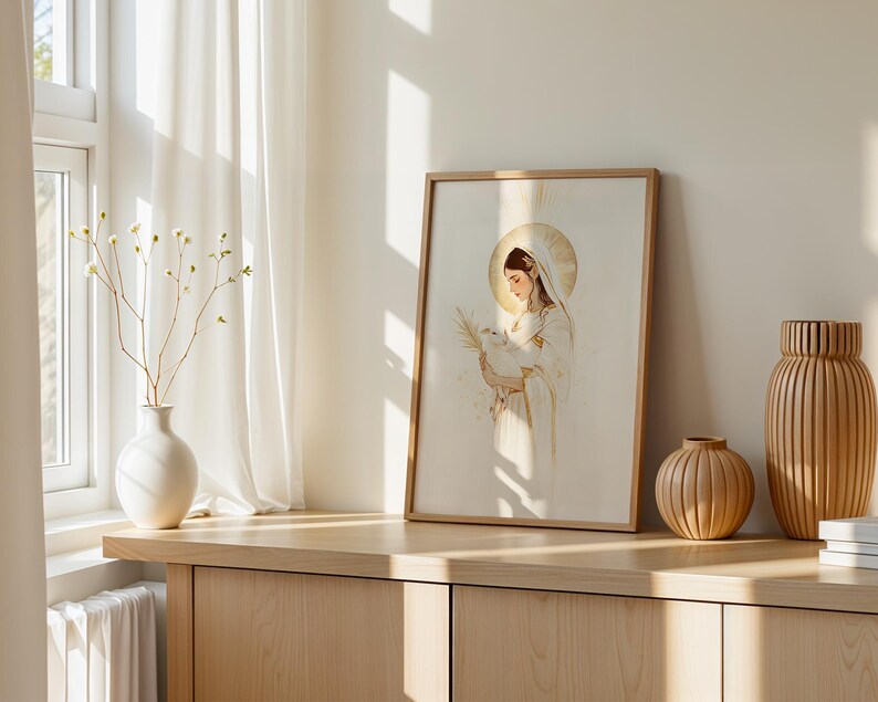 May include: A framed wall art print featuring a stylised illustration of a figure with a golden halo holding a small white lamb and a palm frond. The artwork uses a soft colour palette of cream, white, and gold accents, presented in a light wood frame.