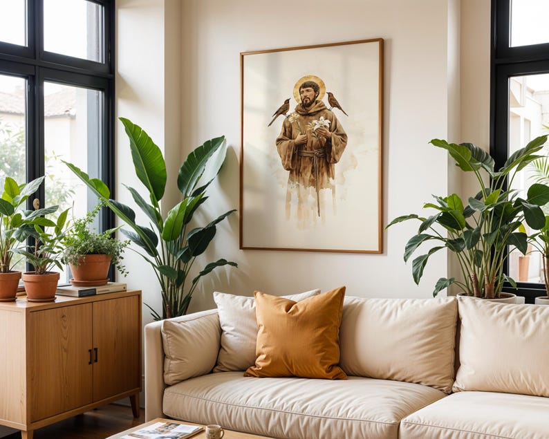 May include: A framed wall art print depicting a figure in a brown hooded robe with a gold halo, holding white flowers with birds perched on each shoulder. The artwork features a soft, watercolor-style aesthetic with muted earth tones and light shading.