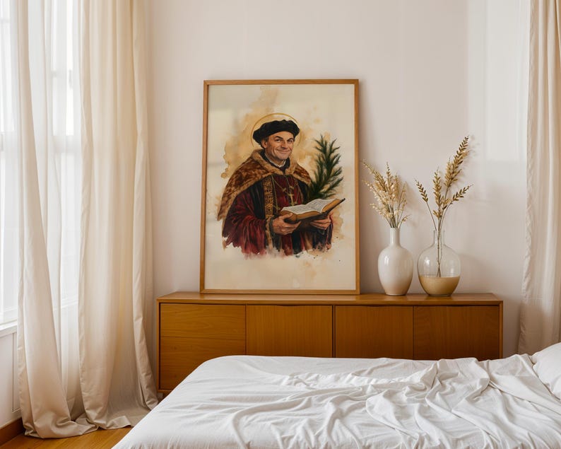 May include: A framed watercolour portrait of a man wearing a dark cap and a maroon robe with gold trim, holding an open book and a green palm frond. The figure has a golden halo around his head, set against a light beige, textured background.