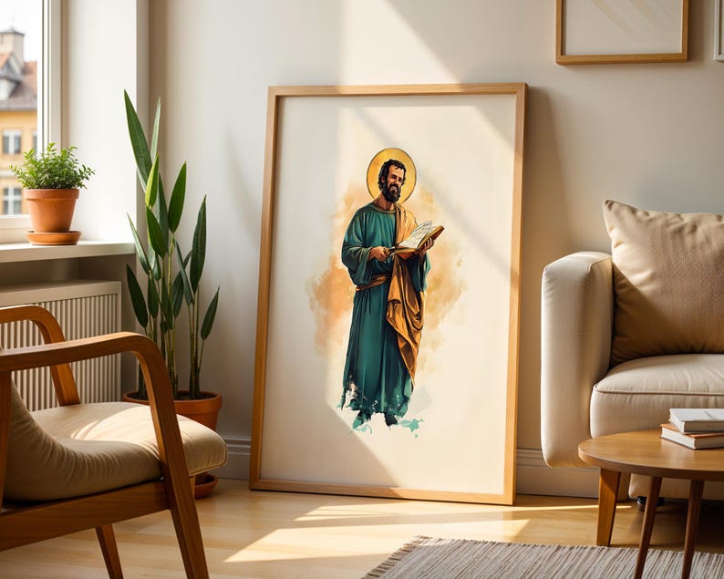 Op de afbeelding: Een ingelijste wandkunstprint met een aquarelillustratie van een bebaard figuur in een blauwgroen gewaad en gouden mantel, die een open boek vasthoudt. Het figuur heeft een gouden halo achter het hoofd tegen een lichte achtergrond.