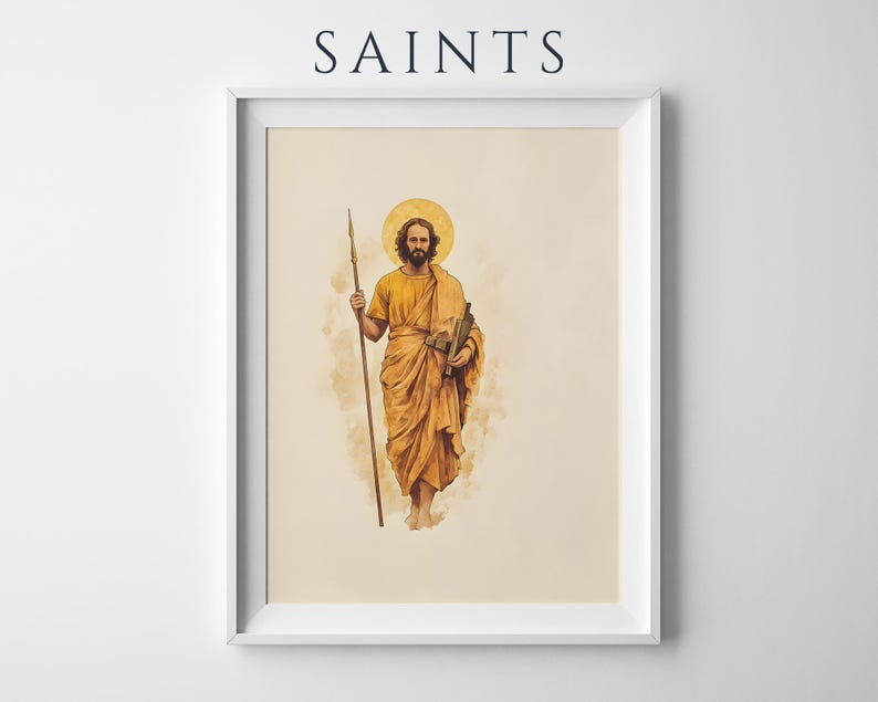 Op de afbeelding: Een ingelijste kunstdruk met de tekst SAINTS bovenaan. Het kunstwerk toont een bebaarde figuur in goudgele gewaden met een aureool, die een lange speer in de rechterhand en een boekrol in de linkerhand houdt, tegen een lichtbeige achtergrond.
