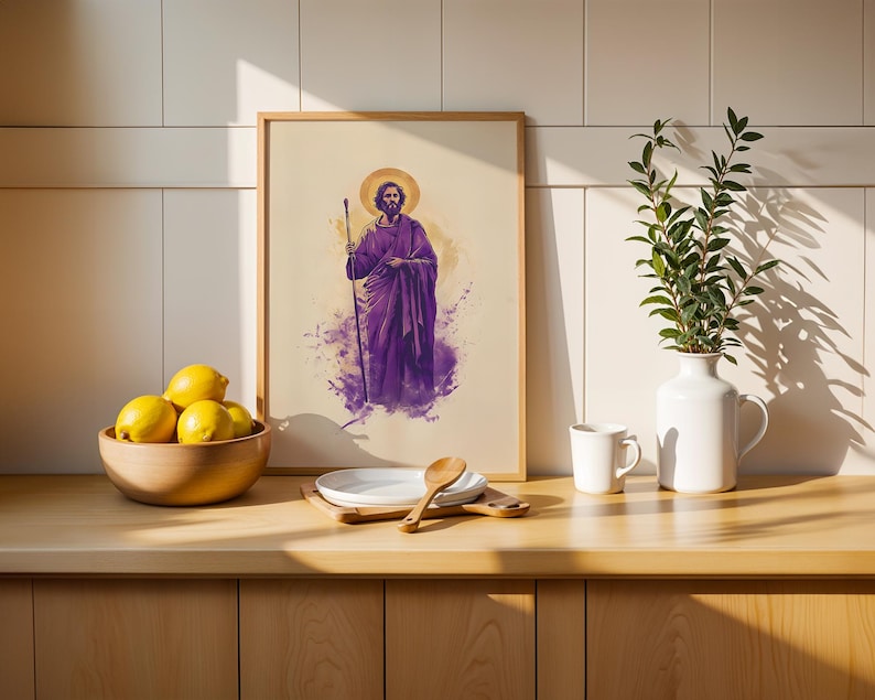 May include: A framed vertical print featuring a bearded figure in a purple robe holding a staff, set against a light background with a golden halo. The artwork is displayed on a wooden counter next to a bowl of yellow lemons and a white vase.