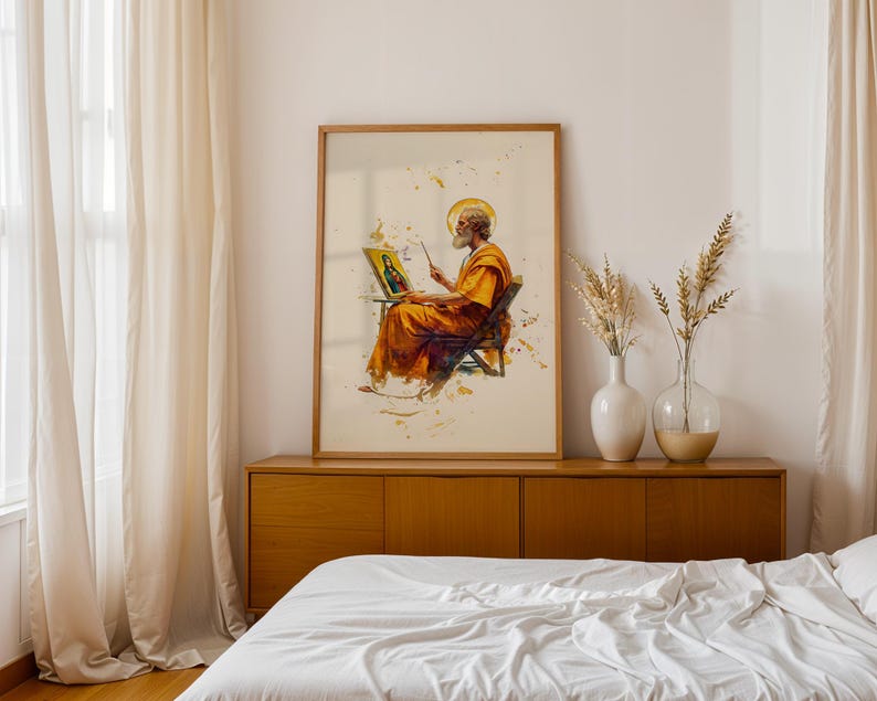 May include: A framed wall art print featuring a watercolour-style illustration of a bearded figure in orange robes sitting on a chair, painting a portrait on an easel. The artwork includes golden splatters and a halo effect around the figure's head.