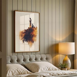 May include: A framed wall art print featuring a silhouette of a figure standing on a rocky cliff edge, with a vibrant orange and dark brown watercolour-style cloud effect beneath the landmass, set against a plain white background.