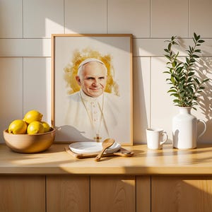 May include: A framed portrait of Pope John Paul II in a watercolour style with a golden halo effect, displayed alongside a wooden bowl of yellow lemons, a white plate with a wooden spoon, a white mug, and a white vase with green leafy branches.