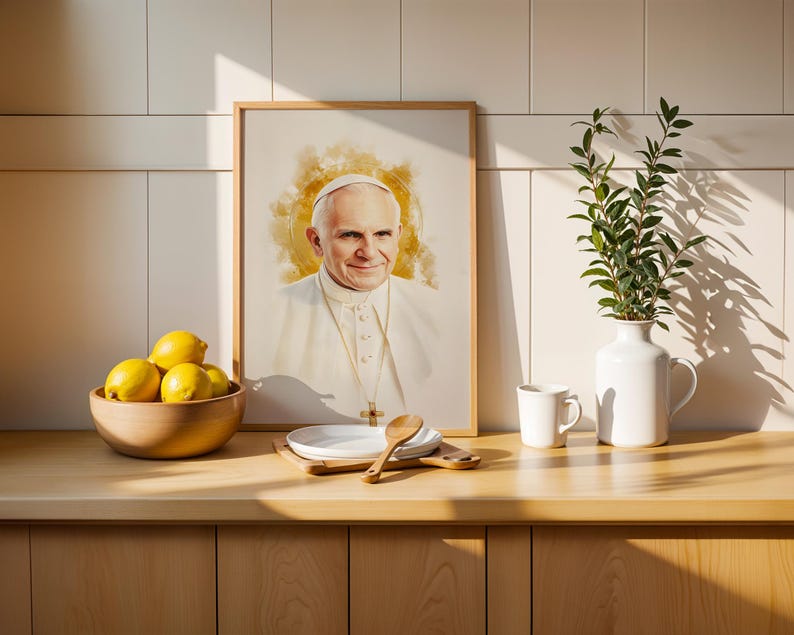 May include: A framed portrait of Pope John Paul II in a watercolour style with a golden halo effect, displayed alongside a wooden bowl of yellow lemons, a white plate with a wooden spoon, a white mug, and a white vase with green leafy branches.