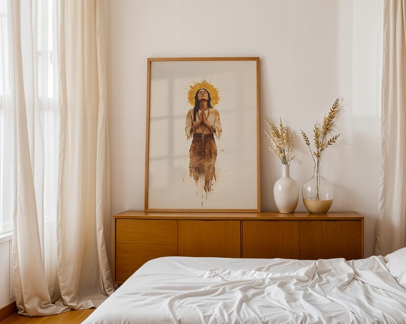 May include: A framed vertical wall art print featuring a watercolour-style illustration of a person with hands pressed together in prayer, wearing a light-coloured top and a dark skirt, with a golden sunburst halo effect behind their head.