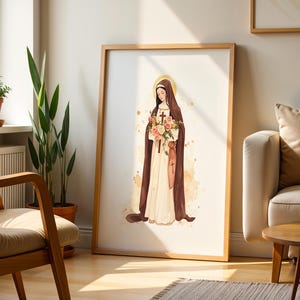 May include: A framed wall art print featuring a watercolor illustration of a figure in a brown habit and white robe, holding a bouquet of pink and white roses with a small cross. The figure has a golden halo and stands against a light background.