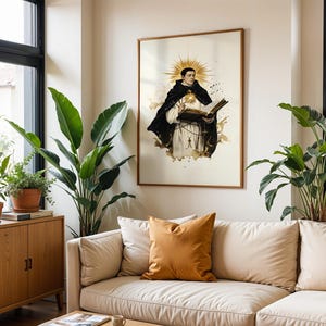 May include: A framed wall art print featuring a central illustration of a figure in a black and white religious habit, holding an open book with a golden sunburst halo behind the head, set against a cream background with ink-like splatters.