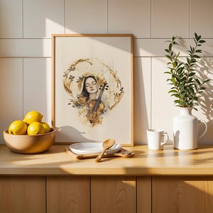 Op de afbeelding: Een ingelijste kunstdruk met een aquarelillustratie van een persoon met gesloten ogen die een viool vasthoudt, omringd door gouden bloemaccenten. De print staat op een houten aanrecht naast een schaal met gele citroenen en een witte vaas.