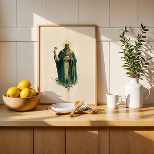 May include: A framed vertical art print featuring a bearded figure in a dark green robe and crown, holding a shamrock and a staff. The print is displayed on a wooden counter next to a wooden bowl of yellow lemons, a white plate, a spoon, and a white vase.