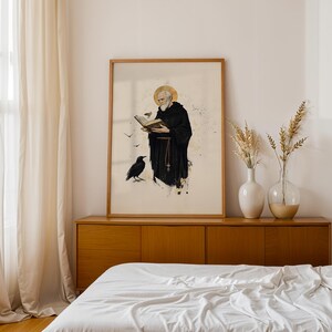 Op de afbeelding: Een ingelijste verticale wandkunstprint met een bebaarde figuur in een zwarte kapmantel die een open boek vasthoudt. Een gouden halo omringt het hoofd en een zwarte raaf staat aan de voeten. De illustratie bevat kleine vogels en inktspatten.