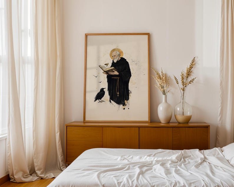 Op de afbeelding: Een ingelijste verticale wandkunstprint met een bebaarde figuur in een zwarte kapmantel die een open boek vasthoudt. Een gouden halo omringt het hoofd en een zwarte raaf staat aan de voeten. De illustratie bevat kleine vogels en inktspatten.