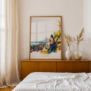May include: A framed vertical wall art print featuring a watercolour-style illustration of a figure with long hair and robes sitting on a hillside, gesturing towards a large crowd gathered below near a body of water, with yellow and blue colour tones.