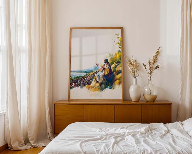 May include: A framed vertical wall art print featuring a watercolour-style illustration of a figure with long hair and robes sitting on a hillside, gesturing towards a large crowd gathered below near a body of water, with yellow and blue colour tones.