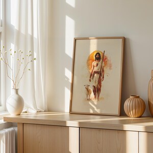 Peut inclure: Une impression encadr&eacute;e de style aquarelle repr&eacute;sentant une silhouette barbue v&ecirc;tue de tissus drap&eacute;s tenant un b&acirc;ton, accompagn&eacute;e d'un petit agneau. L'&oelig;uvre pr&eacute;sente un fond circulaire orange chaud et est dans un cadre en bois clair.