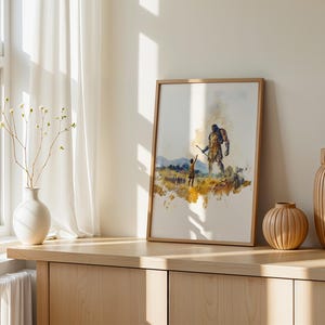 May include: A framed watercolor print featuring a small figure reaching toward a large, towering giant in a golden-hued landscape. The artwork uses expressive brushstrokes in shades of yellow, brown, and blue to depict the scene on a white background.