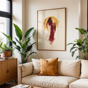 Puede incluir: Una impresi&oacute;n de arte mural enmarcada que muestra una figura con cabello largo y oscuro vistiendo una prenda fluida roja y blanca, frente a un gran halo circular dorado. La obra se exhibe en un marco de madera fino sobre una pared color crema.