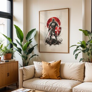 May include: A framed wall art print featuring a knight in full armour standing over a dark creature. The knight holds a sword and a shield with a red cross. A large red circle sits behind the figure, with ink-like splatters in black and red.