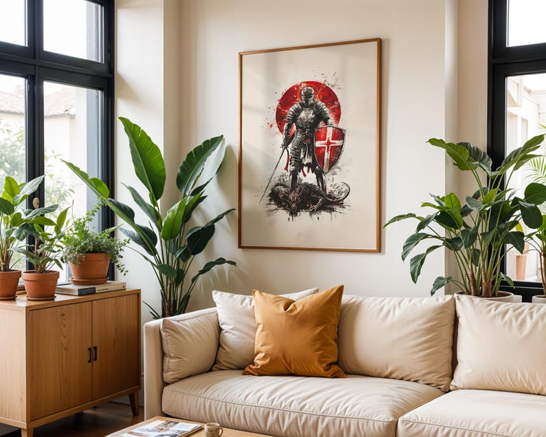 May include: A framed wall art print featuring a knight in full armour standing over a dark creature. The knight holds a sword and a shield with a red cross. A large red circle sits behind the figure, with ink-like splatters in black and red.