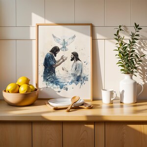 Peut inclure: Une impression encadr&eacute;e de style aquarelle repr&eacute;sentant une sc&egrave;ne de bapt&ecirc;me avec deux personnages dans l'eau et une colombe blanche au-dessus, pr&eacute;sent&eacute;e dans une cuisine avec un bol de citrons jaunes, une cuill&egrave;re en bois et un vase blanc.
