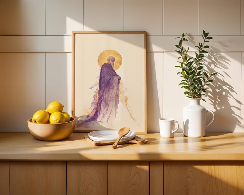 May include: A framed art print featuring a figure in a purple robe with a golden halo, displayed on a wooden counter next to a bowl of yellow lemons, a stack of white plates with a wooden spoon, a white mug, and a white vase with green leaves.