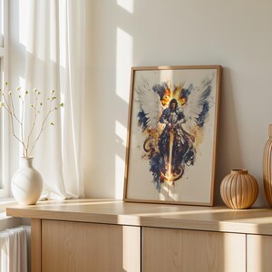 May include: A framed vertical art print featuring a watercolour-style illustration of a winged warrior in armour holding a sword. The artwork displays a central figure with large white wings, surrounded by splashes of orange, yellow, and dark blue ink.