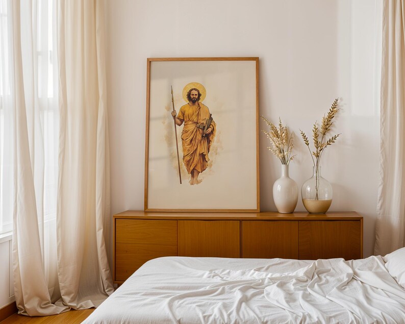 Op de afbeelding: Een ingelijste verticale wandkunstprint met een aquarelillustratie van een bebaard figuur met een gouden halo, gekleed in okerkleurige gewaden, met een lange houten staf in de rechterhand en een boek in de linkerhand.