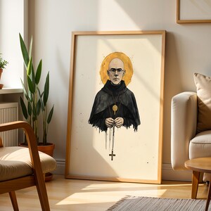 May include: A framed art print featuring a bald person with glasses wearing a black hooded robe. A golden halo circles the head, and a gold pendant hangs from the neck. The person holds a rosary with a cross, rendered in a watercolor style.