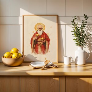 May include: A framed wall art print featuring a watercolour illustration of a bearded figure in red robes with a golden halo, holding two golden spheres. The artwork is displayed in a light wood frame with a cream-coloured background and paint splatters.