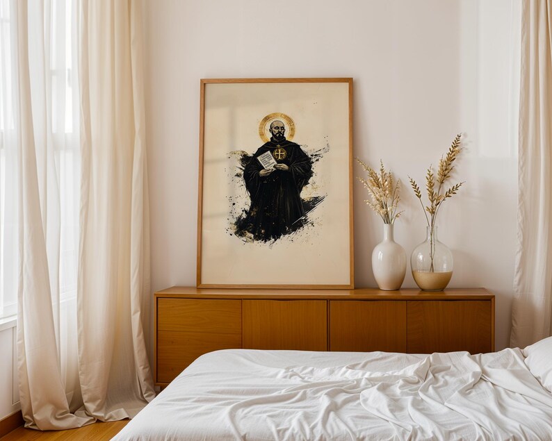 May include: A framed wall art print featuring a bald monk in a black habit with a gold halo, holding a white scroll with text. The artwork uses black ink splatters and gold accents on a light background, presented in a simple wooden frame.