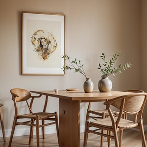 Op de afbeelding: Een ingelijste kunstdruk met een aquarelillustratie van een persoon met gesloten ogen die een viool vasthoudt, omringd door gouden bloemaccenten. Het kunstwerk hangt in een kamer met een houten eettafel, stoelen en twee keramische vazen.
