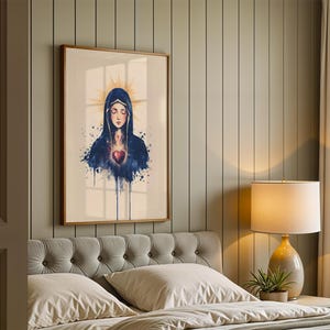 K&ouml;nnte beinhalten: Ein gerahmter Kunstdruck mit einer Aquarell-Illustration einer Figur mit geschlossenen Augen, die einen dunkelblauen Kapuzenumhang tr&auml;gt, mit einem leuchtenden goldenen Heiligenschein hinter dem Kopf und einem leuchtend roten Herz auf der Brust.