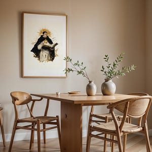 May include: A framed wall art print depicting a figure in a black and white habit holding an open book with a golden sunburst halo behind the head, displayed in a dining room with a wooden table, four chairs, and two ceramic vases with greenery.