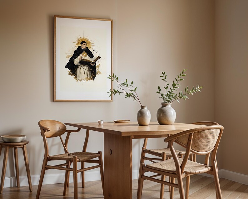 May include: A framed wall art print depicting a figure in a black and white habit holding an open book with a golden sunburst halo behind the head, displayed in a dining room with a wooden table, four chairs, and two ceramic vases with greenery.