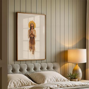 May include: A framed wall art print featuring a watercolour-style illustration of a person with hands pressed together in a prayer gesture, surrounded by a golden sunburst halo, wearing a light-coloured top and a textured brown skirt.