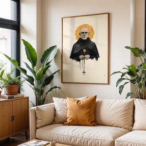 May include: A framed wall art print featuring a bald person wearing glasses and a black hooded robe with a gold halo behind their head. The person holds a rosary with a cross pendant hanging down. The illustration is set against a cream background.