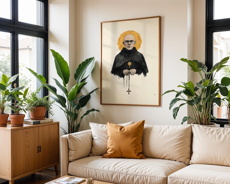 May include: A framed wall art print featuring a bald person wearing glasses and a black hooded robe with a gold halo behind their head. The person holds a rosary with a cross pendant hanging down. The illustration is set against a cream background.