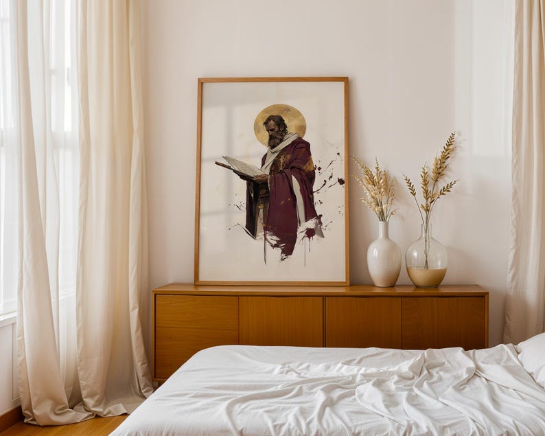 Op de afbeelding: Een ingelijste verticale kunstprint met een bebaarde figuur in een dieppaarse mantel met een gouden halo, lezend in een open boek. Het kunstwerk gebruikt een aquarel-stijl met inktspatten op een witte achtergrond, in een lichthouten lijst.