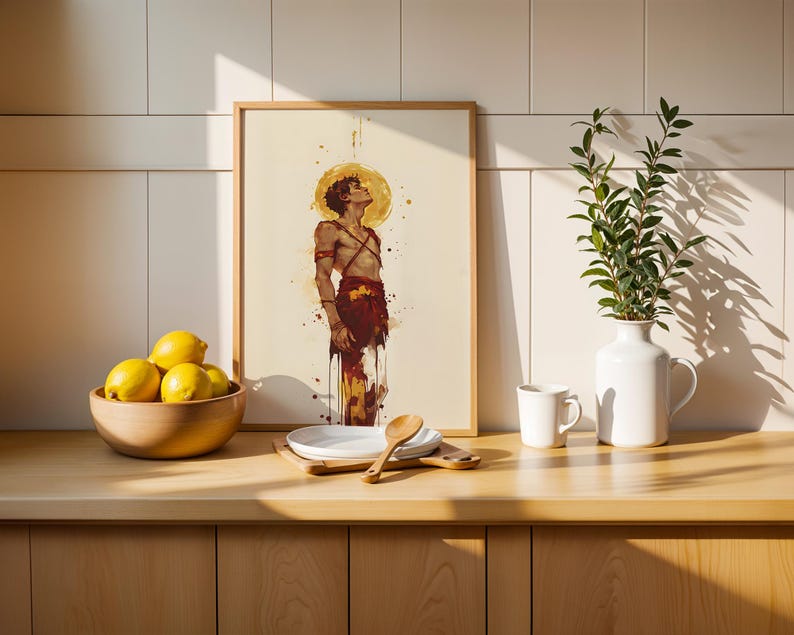May include: A framed art print featuring a watercolour-style illustration of a person looking upward with a golden halo, displayed on a wooden counter next to a bowl of yellow lemons, a white plate, a wooden spoon, a white mug, and a white vase.