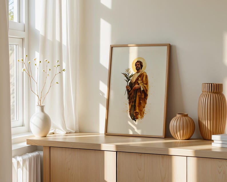 K&ouml;nnte beinhalten: Ein gerahmter vertikaler Druck, der eine b&auml;rtige Figur in einem goldbraunen Gewand mit einem bl&uuml;henden Zweig zeigt, dargestellt mit einem kreisf&ouml;rmigen Heiligenschein hinter dem Kopf auf hellem cremefarbenem Grund in einem hellen Holzrahmen.