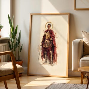 Puede incluir: Una l&aacute;mina de arte enmarcada con una ilustraci&oacute;n en acuarela de una figura sonriente vestida con una armadura de inspiraci&oacute;n romana antigua y una capa de color rojo oscuro, sosteniendo una espada, con un halo dorado sobre la cabeza.