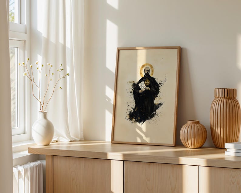 May include: A framed vertical art print featuring a bearded figure in a black robe with a gold halo, holding a white document with text. The illustration uses black ink splatters on a cream background, presented in a light wood frame.