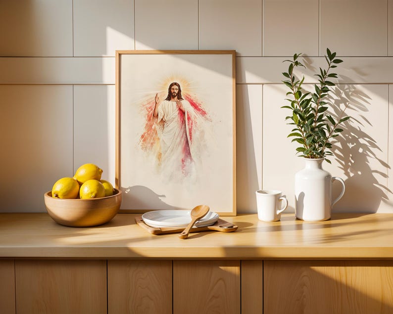 May include: A framed watercolor-style print depicting a figure in white and red robes with a glowing halo, positioned on a wooden counter next to a bowl of yellow lemons, a white ceramic pitcher with green leaves, and a small wooden spoon.