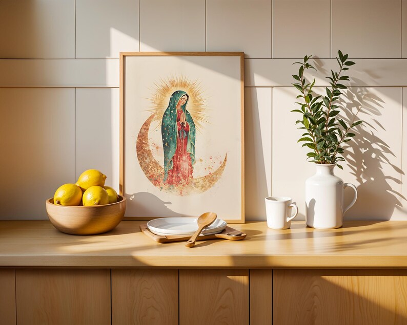 May include: A framed wall art print featuring a watercolor illustration of the Virgin of Guadalupe standing on a crescent moon with a golden sunburst halo, displayed on a wooden counter next to a bowl of yellow lemons and a white ceramic vase.