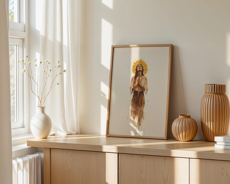 May include: A framed vertical wall art print featuring a watercolour illustration of a person with long dark hair, hands pressed together in prayer, and a golden sunburst halo behind their head, rendered in earthy brown and tan tones.