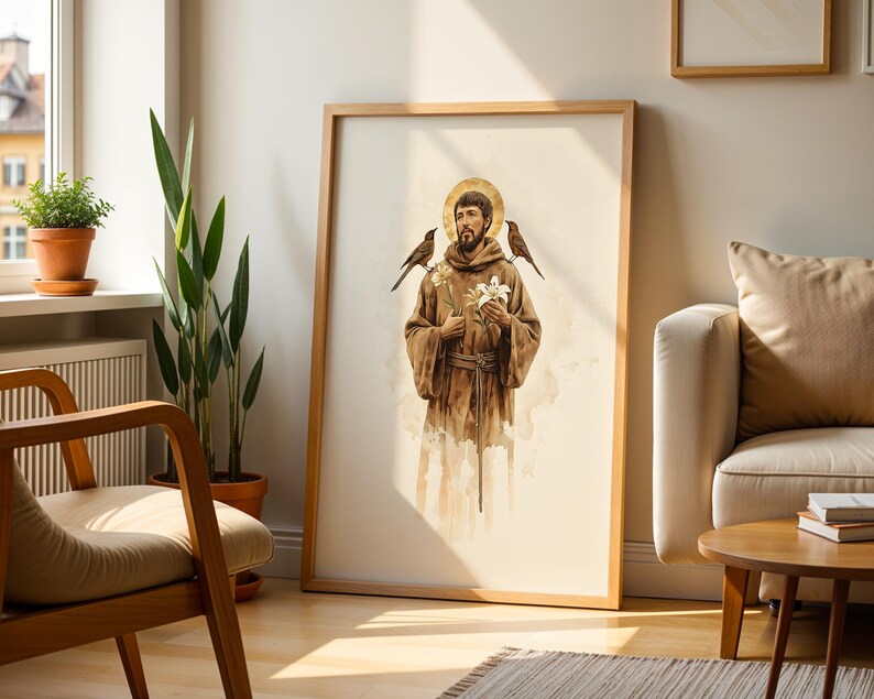 May include: A framed wall art print featuring a watercolour illustration of a bearded figure in a brown robe with a golden halo, holding a white lily, with two small birds perched on the shoulders, set against a light cream background.