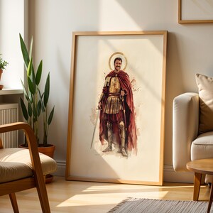 Puede incluir: Una l&aacute;mina de arte enmarcada con una ilustraci&oacute;n en acuarela de una figura sonriente vestida con una armadura de inspiraci&oacute;n romana antigua y una capa de color rojo oscuro, sosteniendo una espada, con un halo dorado sobre la cabeza.