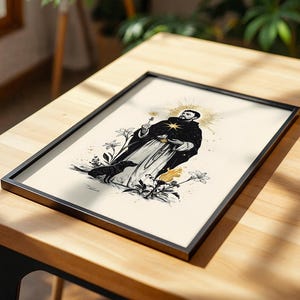 May include: A framed rectangular print featuring a black and white illustration of a robed figure with a golden halo, holding a small object. A small dog stands near the figure, surrounded by stylised lilies and a flame on a cream background.
