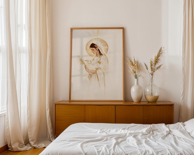 May include: A framed vertical wall art print featuring a watercolour-style illustration of a figure with a golden halo holding a small white lamb. The artwork is displayed in a light wood frame, resting on a wooden sideboard next to two glass vases.